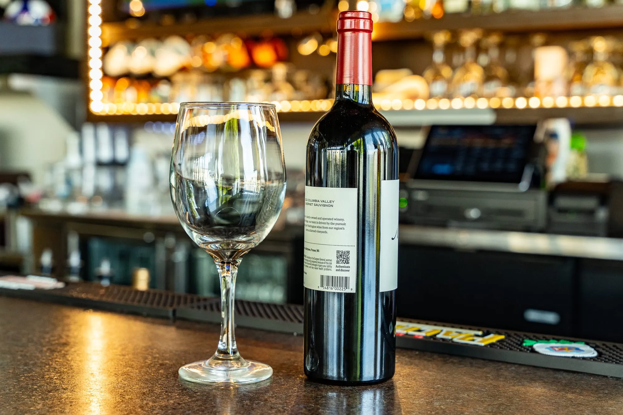 A bottle of red wine and two glasses on the Cozumel bar with warm, glowing light behind