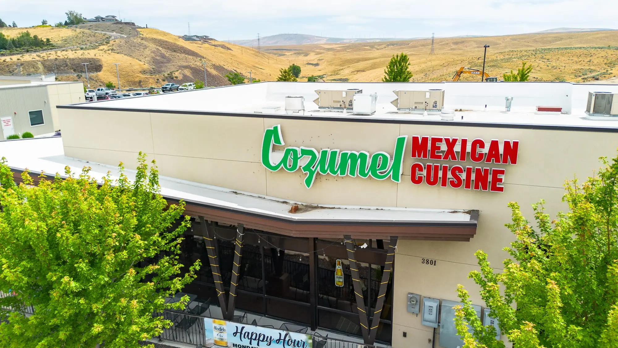 Close-up of the Cozumel Mexican Cuisine building facade with the green script logo and a Happy Hour sign